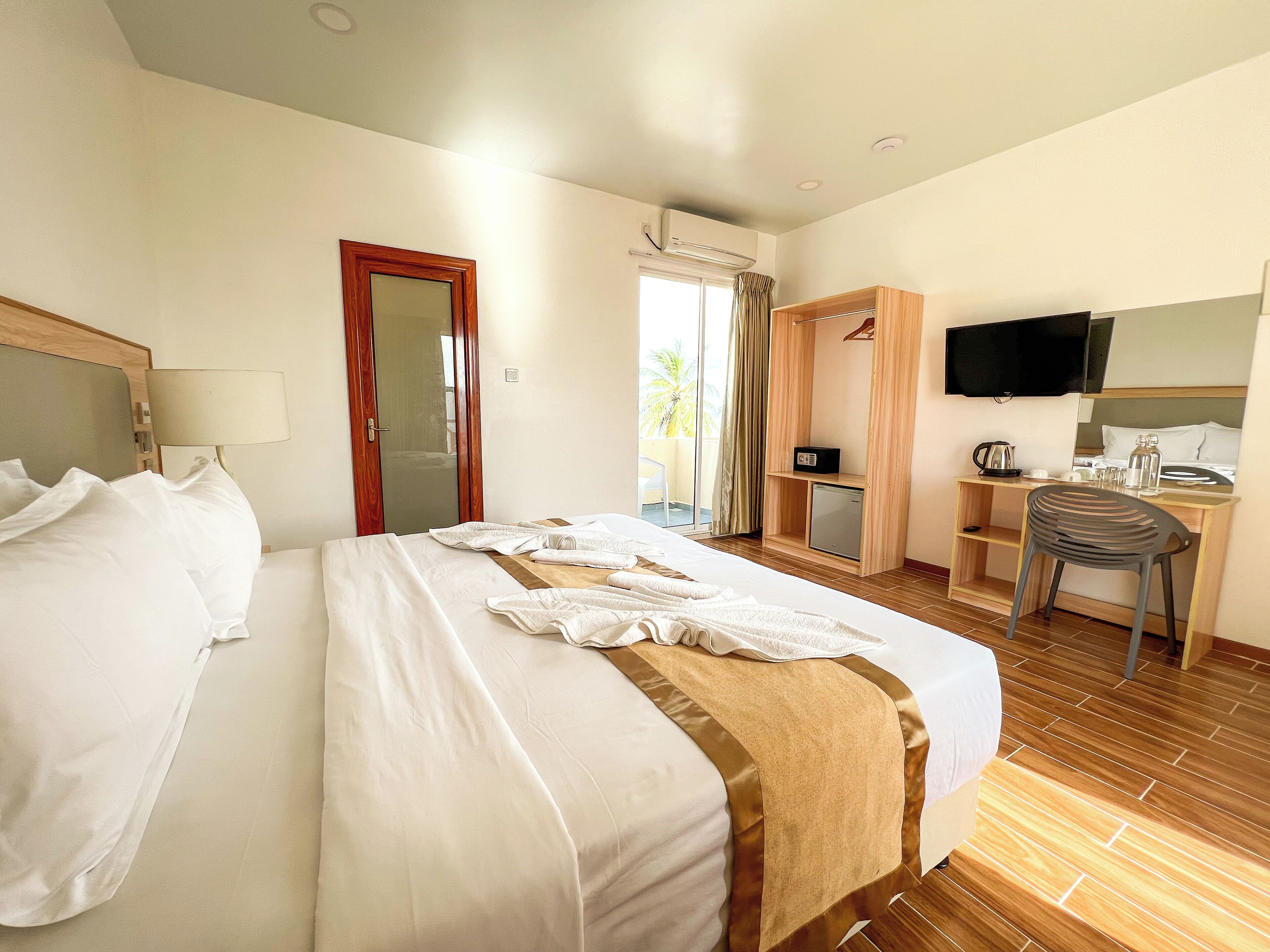 Una habitación de hotel con una cama grande, un escritorio con una silla, televisión y un refrigerador pequeño.