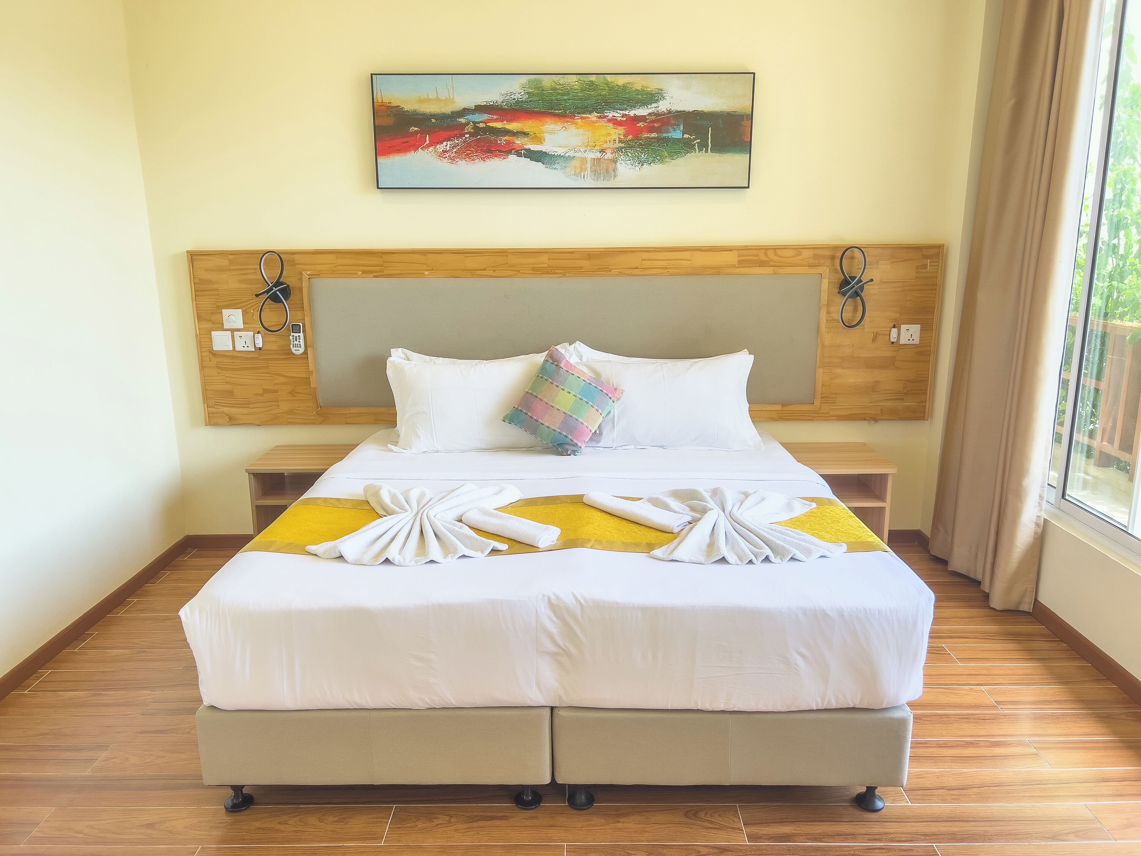 Una cama bien hecha con sábanas blancas, una almohada colorida y toallas dispuestas sobre la cama.