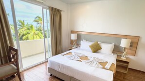 A hotel room with a bed, two bedside tables with lamps, a chair, and a view of palm trees through a sliding glass door. - Rehendhi Villa (Maafushi)