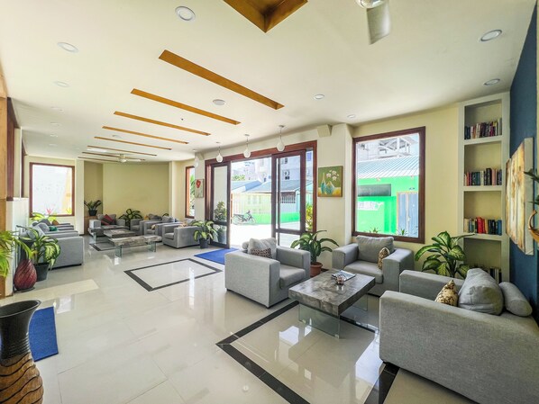A spacious lobby with multiple seating areas, a coffee table, and a bookshelf. - Rehendhi Villa (Maafushi)