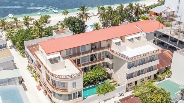 A multi-story hotel with a swimming pool, located near a beach with palm trees and boats. - Rehendhi Villa (Maafushi)