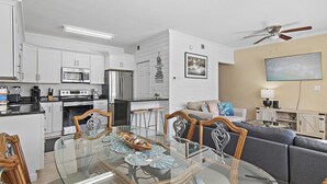 A modern kitchen with white cabinetry, a microwave, and a refrigerator. There is a dining table with chairs and a glass top.