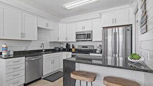 A modern kitchen with white cabinets, stainless steel appliances, a granite countertop, and two wooden stools.