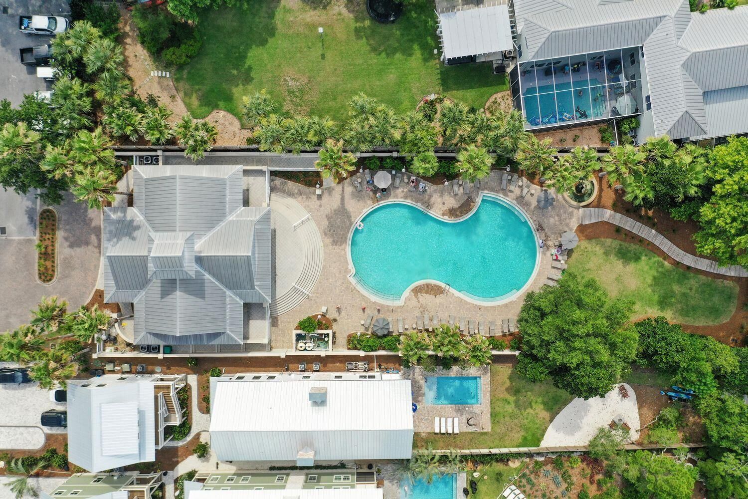 An aerial view of a residential area with a large swimming pool, multiple buildings, and lush greenery.