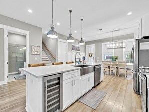 A modern kitchen with a central island, stainless steel appliances, pendant lighting, and a view to the dining area. - Grande Pointe 142- Livesea 30A (Panama City Beach)