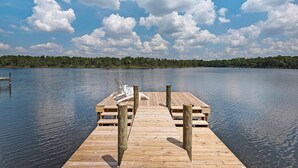 Une jetée en bois s’étendant sur une étendue d’eau calme, avec un ciel dégagé et des arbres en arrière-plan.