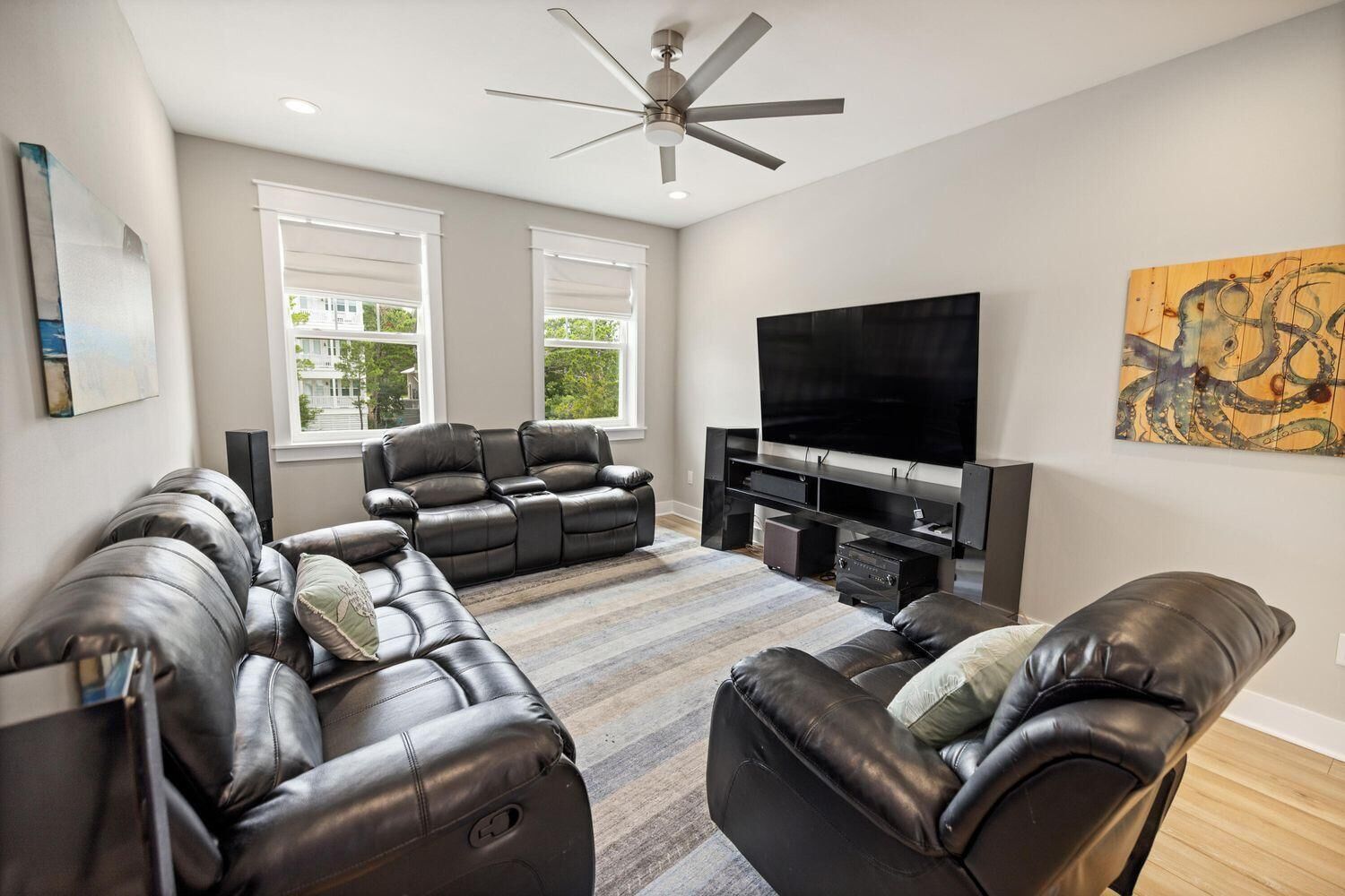 A modern living room with leather sofas, a flat-screen TV, and a ceiling fan.