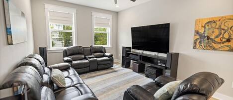 A modern living room with leather sofas, a flat-screen TV, and a ceiling fan.
