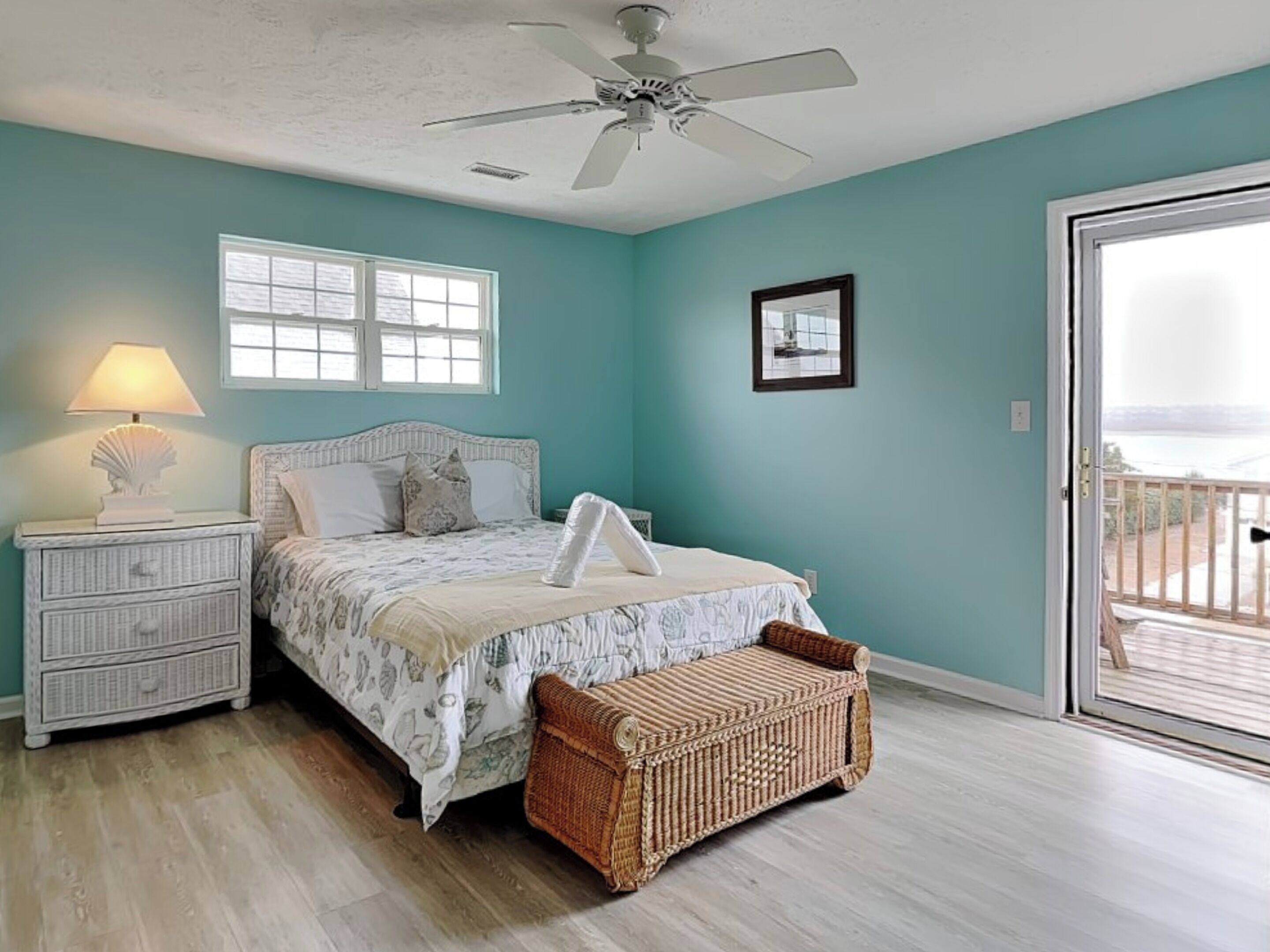 A bedroom with a bed, nightstand, lamp, and a wicker bench.