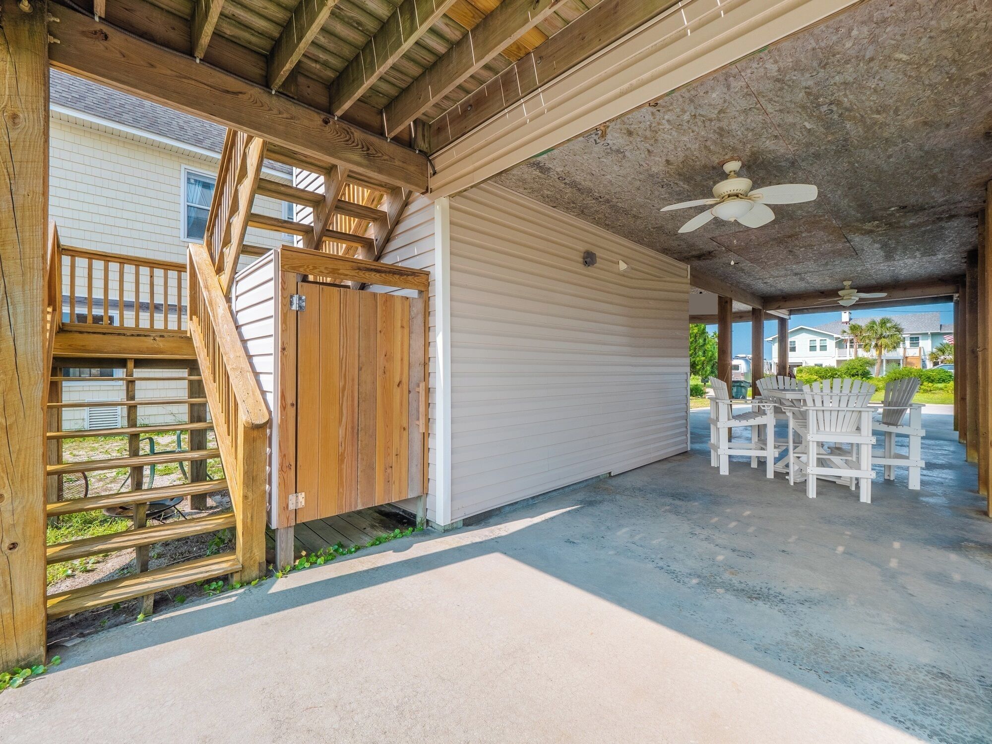 A covered outdoor area with a concrete floor, wooden staircase, and a white garage door.