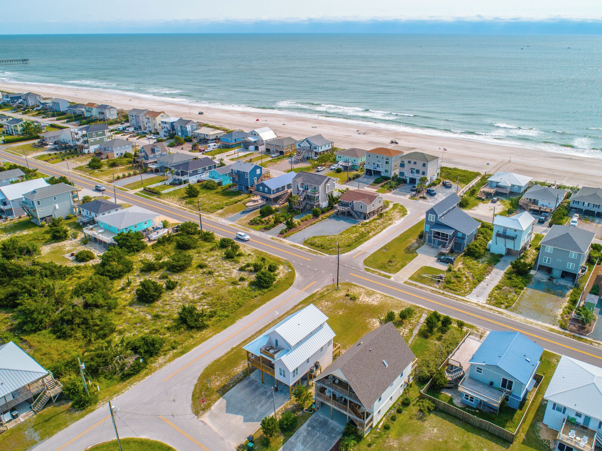Vue aérienne d’une zone résidentielle côtière, avec des maisons, des routes et une plage.