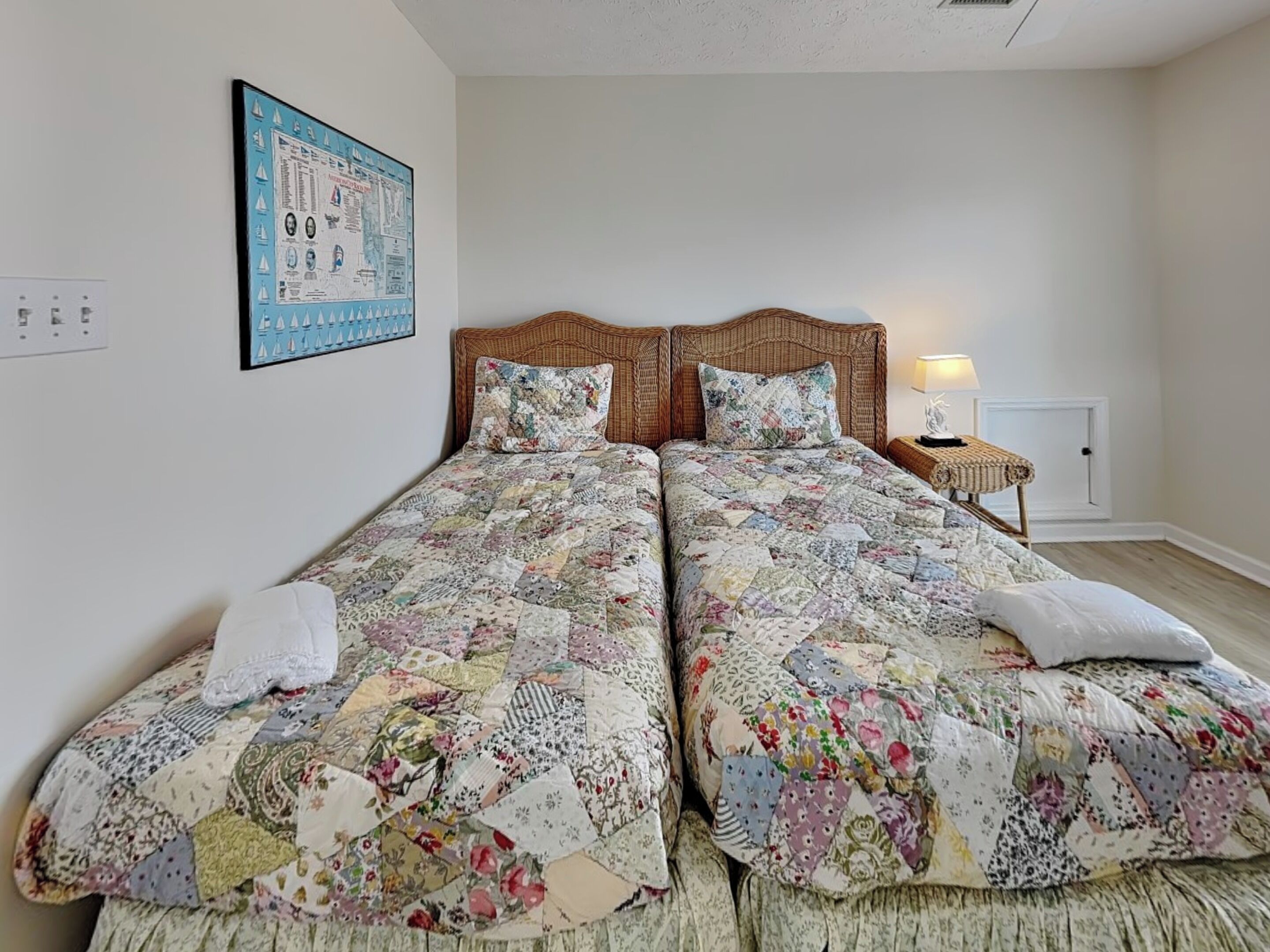 Una cama doble con colcha floral, una mesita de noche con lámpara y un mapa enmarcado en la pared.