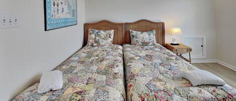 Una cama doble con colcha floral, una mesita de noche con lámpara y un mapa enmarcado en la pared.
