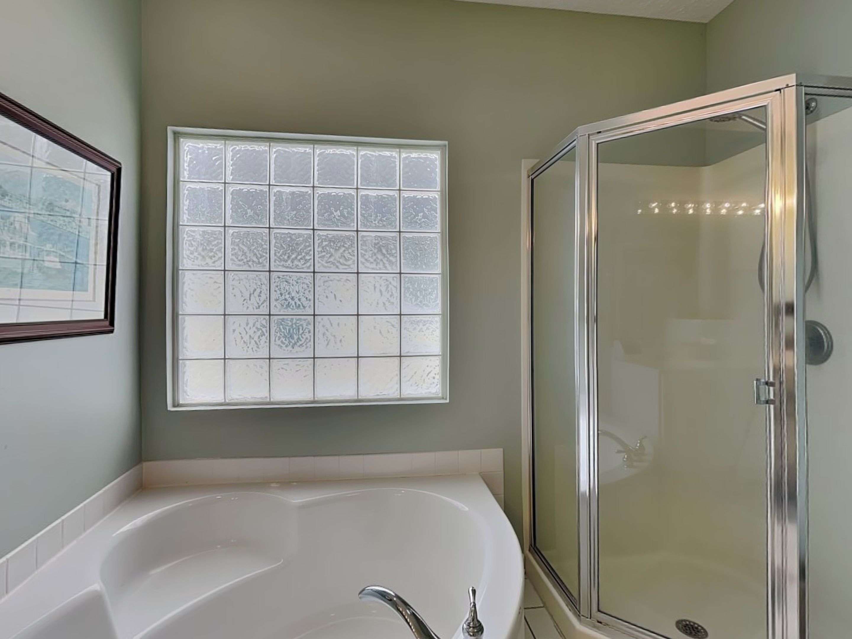 Une salle de bain équipée d’une baignoire, d’un espace douche et d’une fenêtre en verre dépoli.