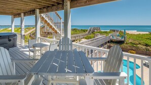 A covered outdoor deck with a pool, white chairs, and a table. - Shore Therapy by Topsail Realty (Sneads Ferry)