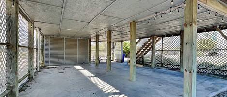 An open covered patio area with concrete flooring and wooden pillars, featuring a lattice fence and a view of the surrounding area.