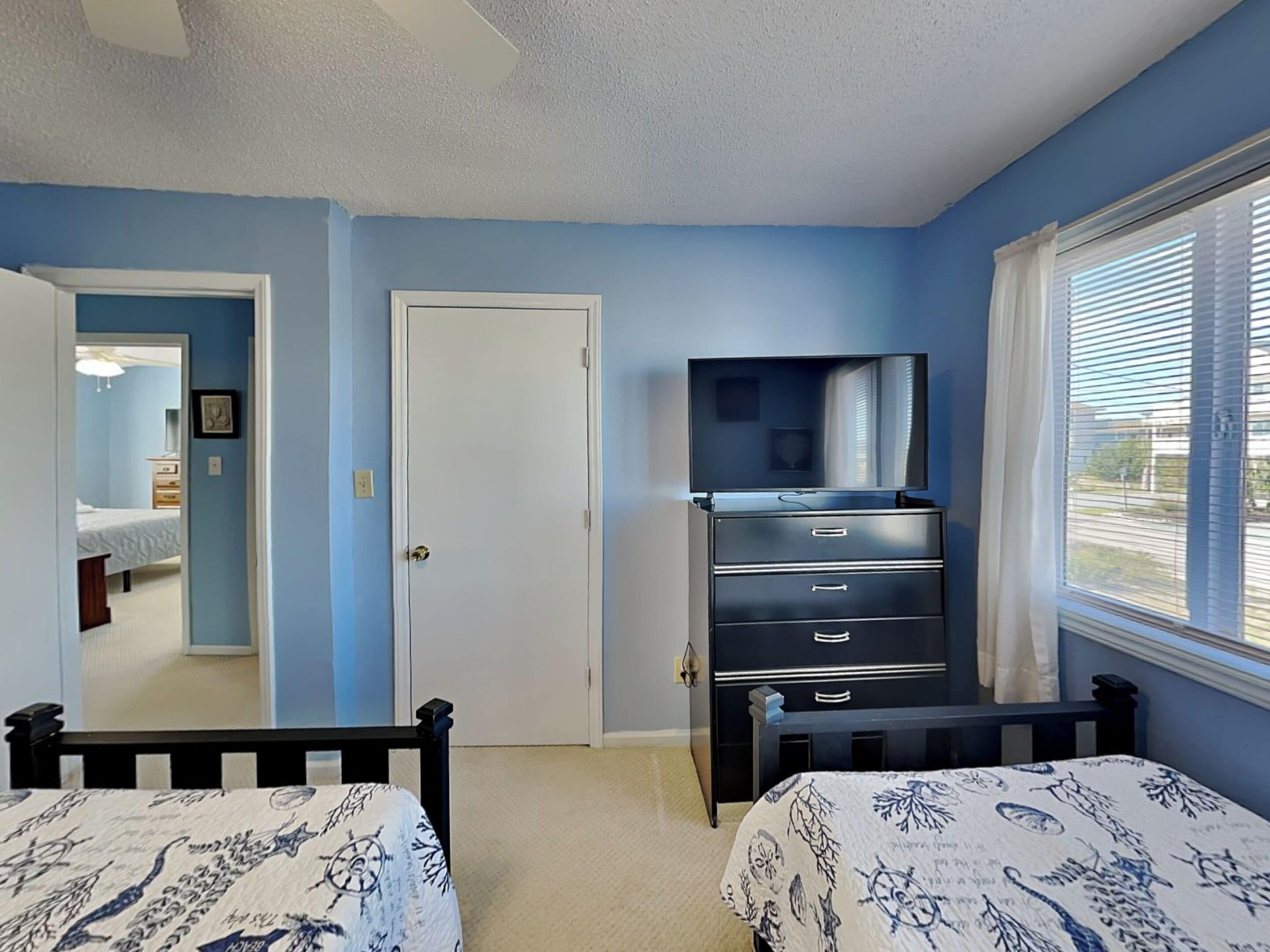 A bedroom with two beds, a dresser, a television, and a window with blinds.