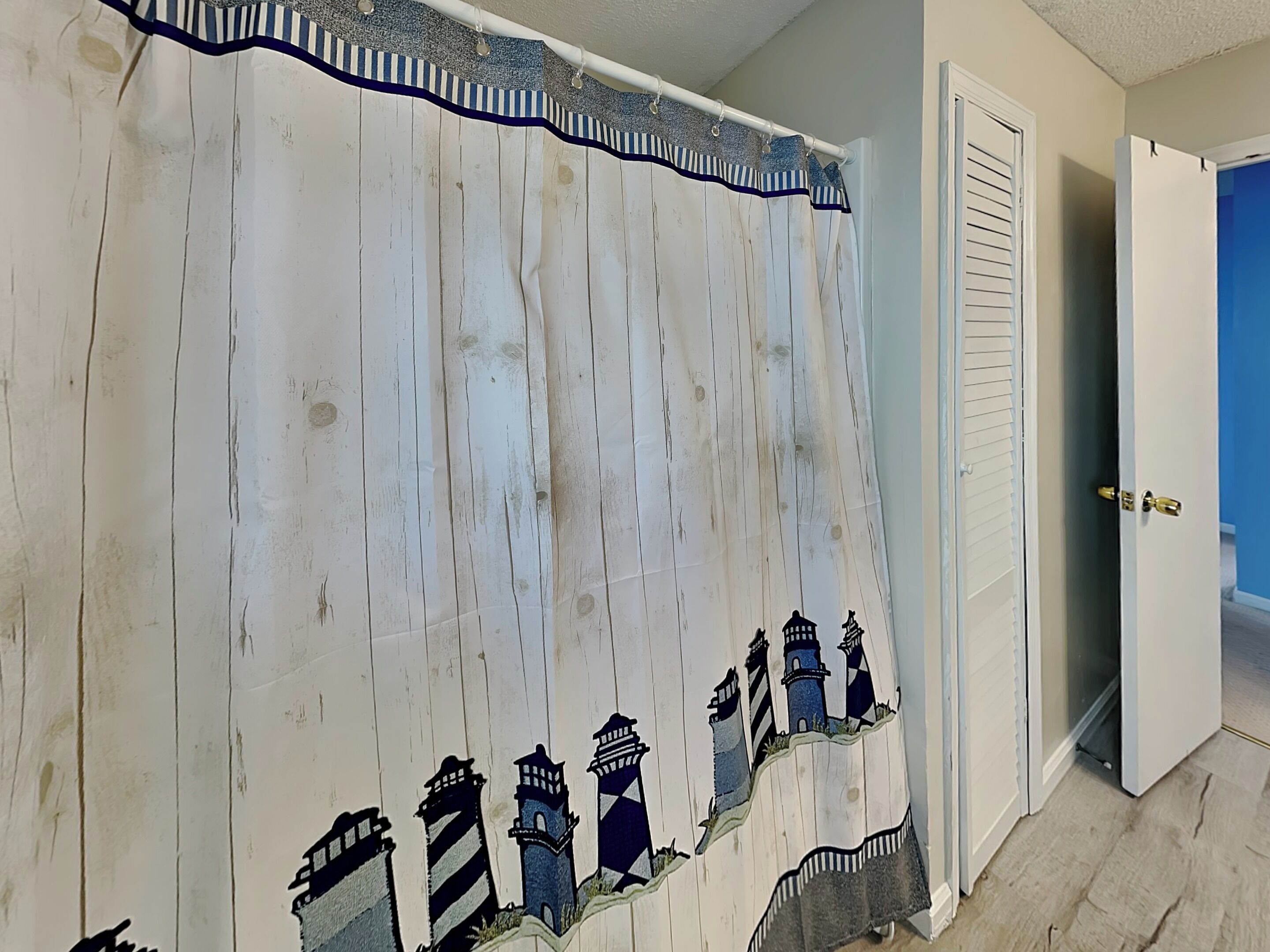 A room with a white curtain featuring a lighthouse design, a door with a gold handle, and a blue wall.