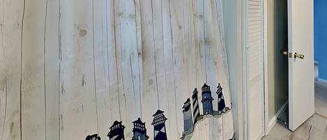 A room with a white curtain featuring a lighthouse design, a door with a gold handle, and a blue wall.