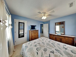 A bedroom with a bed, dresser, mirror, ceiling fan, and a door leading to another room. - Beach Around & Find Out by Topsail Realty (Holly Ridge)