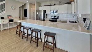 A modern kitchen with a large island, stainless steel appliances, and white cabinetry. - Sea the Love by Topsail Realty (Sneads Ferry)