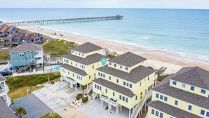 A coastal hotel with multiple buildings, a beach, and a pier in the background. - Sea the Love by Topsail Realty (Sneads Ferry)