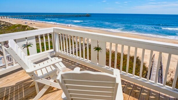 A wooden deck with white railings, a beach view, and a pier in the distance. - Sea the Love by Topsail Realty (Sneads Ferry)
