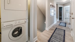 A laundry room with stacked washers and dryers, a hallway with a rug, and a staircase. - Hypnautical by Topsail Realty (Holly Ridge)