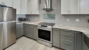 A modern kitchen with stainless steel appliances, grey cabinets, and a herringbone tile backsplash. - Hypnautical by Topsail Realty (Holly Ridge)