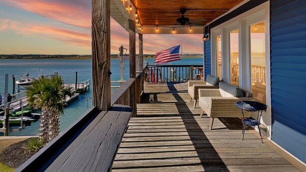 A wooden deck with outdoor furniture, a view of the water, and an American flag.