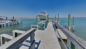 A wooden pier leading to a boat docked at a marina with clear skies.