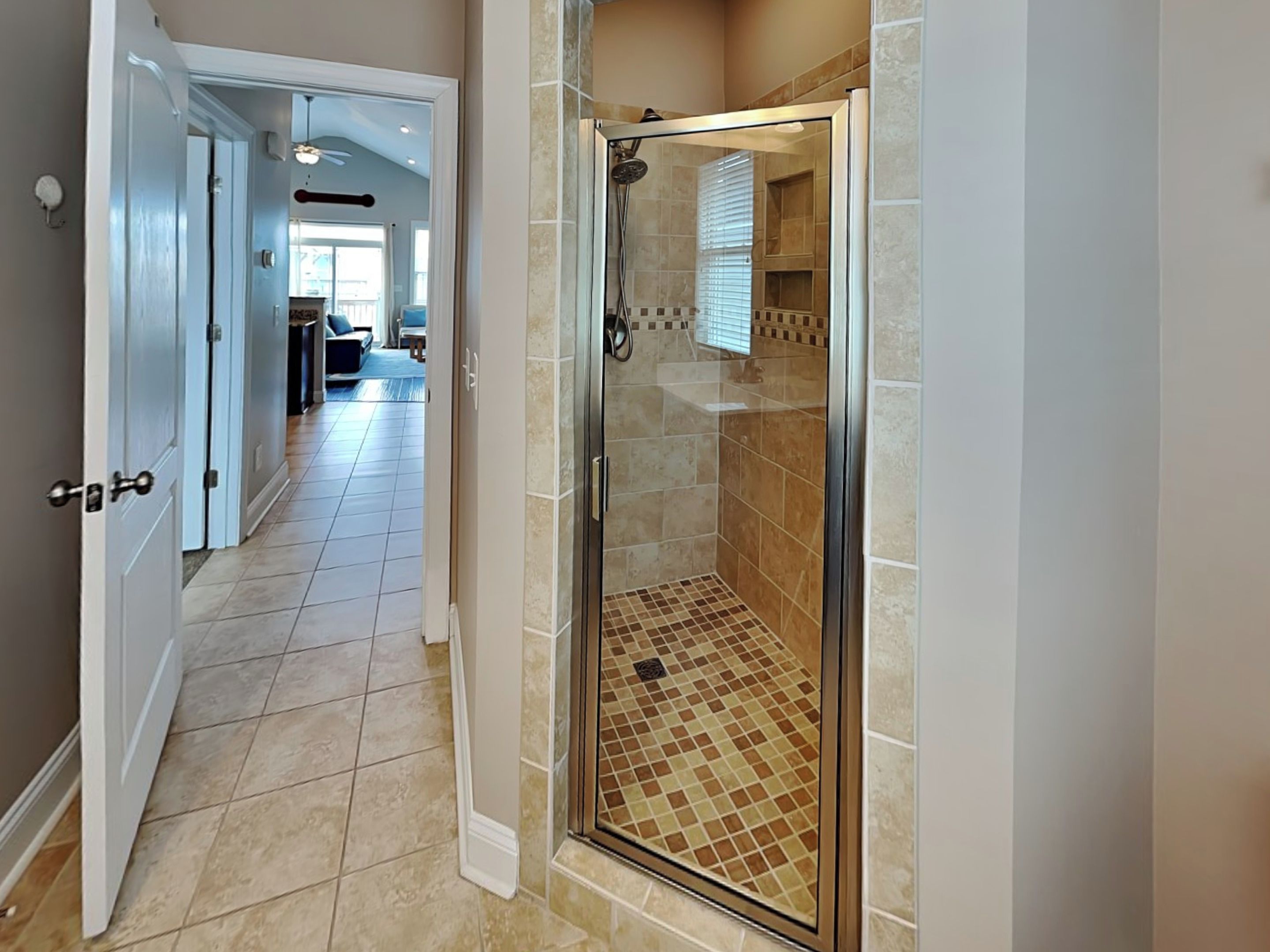 Une salle de bain moderne avec une douche à parois de verre, un carrelage au sol et une pomme de douche visible.