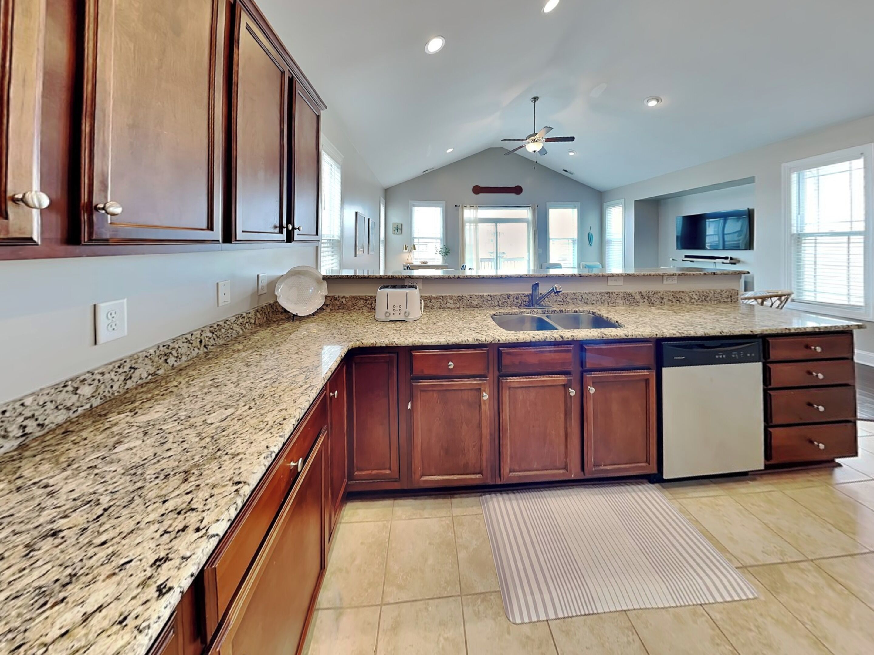 A spacious kitchen with granite countertops, wooden cabinets, a dishwasher, and a large island with a sink.