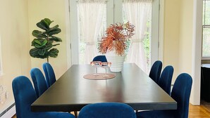 A dining area with a dark wooden table, six blue upholstered chairs, a chandelier, a potted plant, and a vase with dried flowers. - Sleeps 12/Mid-Century Cool/Minutes to Stadium (State College)