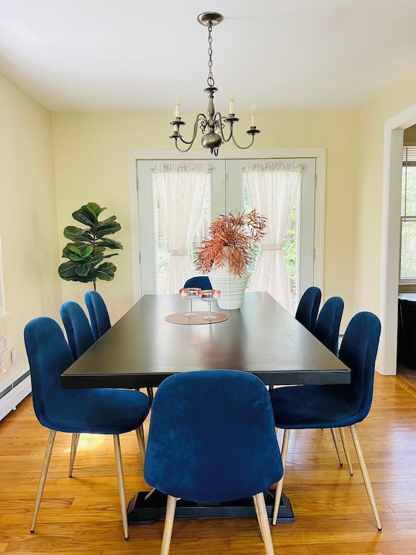 A dining area with a dark wooden table, six blue upholstered chairs, a chandelier, a potted plant, and a vase with dried flowers.