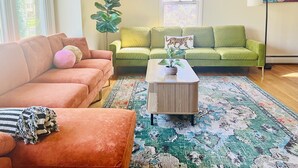 A living room with a green sofa, a pink sofa, a coffee table, and a large plant. - Sleeps 12/Mid-Century Cool/Minutes to Stadium (State College)