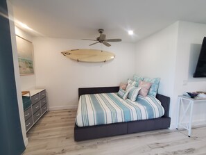 Un dormitorio con cama, ventilador de techo, una tabla de surf y televisor.