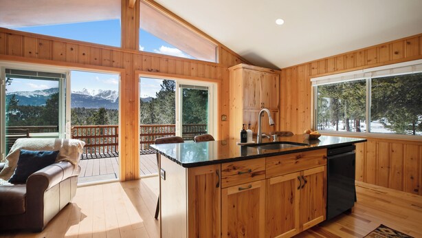 Una cocina amplia con armarios de madera, encimera negra y vistas a montañas a través de amplios ventanales.