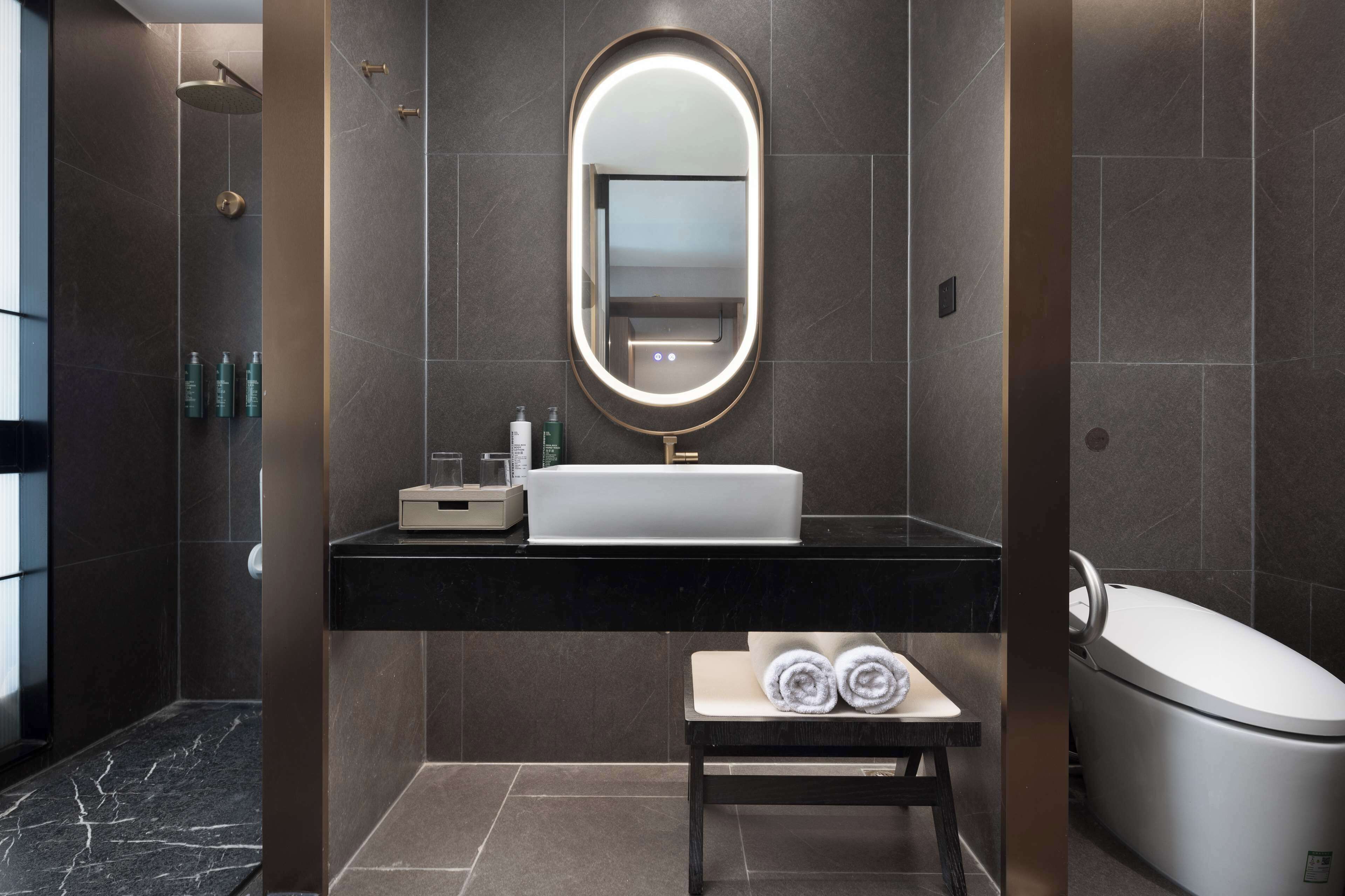 A modern bathroom with a large mirror, a sink, a vanity, a towel rack, and a shower area.