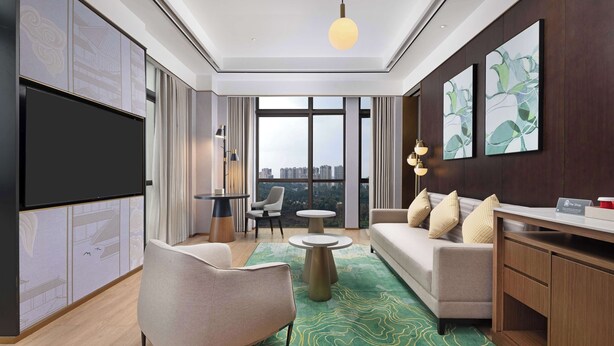 A modern living room with a sofa, armchair, coffee table, and artwork on the wall. - Hilton Garden Inn Leshan Shizhong (Leshan)