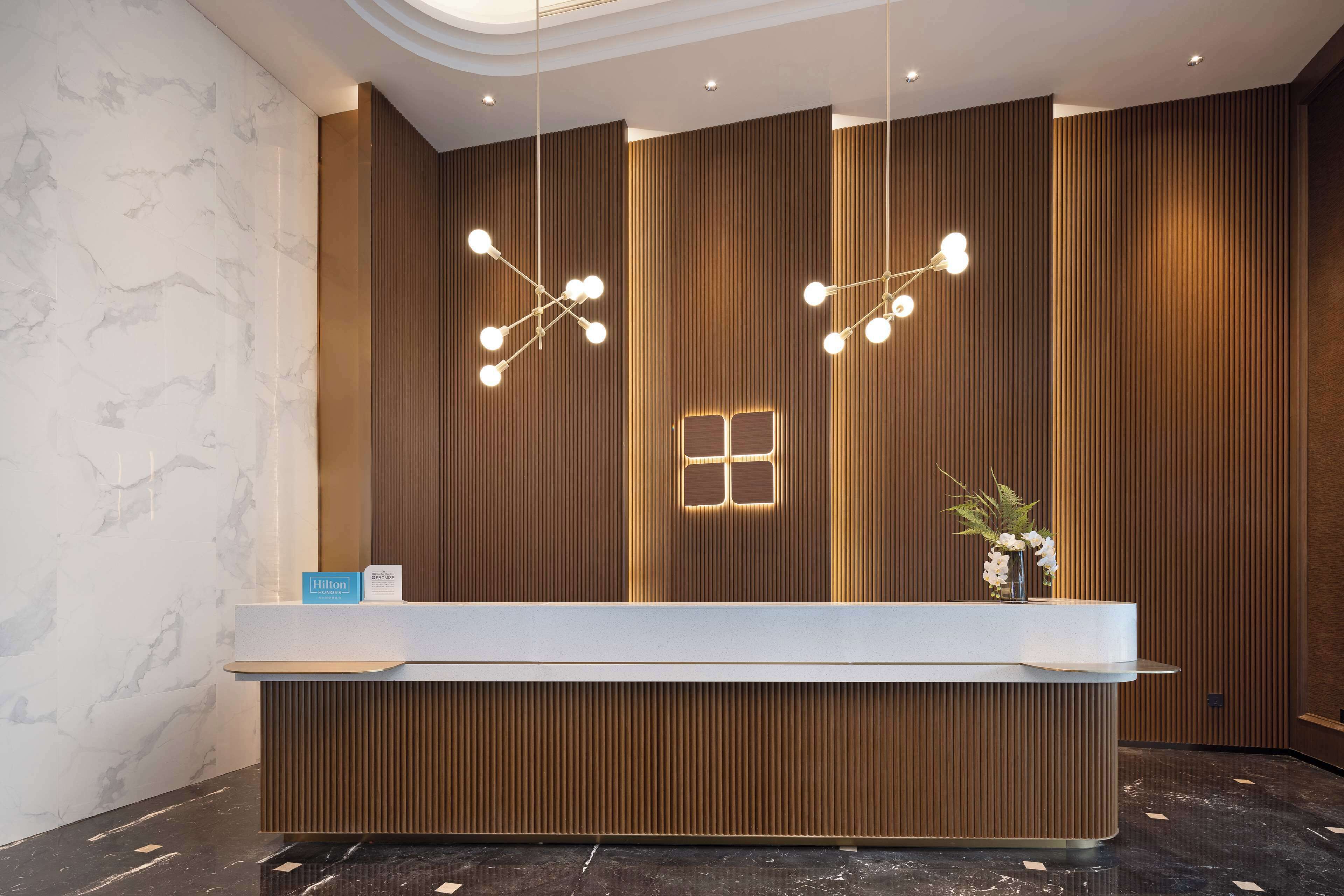 A hotel reception desk with a modern design, featuring a marble wall, wooden paneling, and contemporary lighting fixtures.