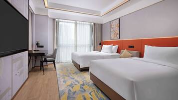 A hotel room with two beds, a desk with a chair, a flat-screen TV, and a large window with curtains.