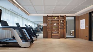 A modern gym with treadmills, a wooden reception desk, and a wall-mounted information board. - Hilton Garden Inn Leshan Shizhong (Leshan)