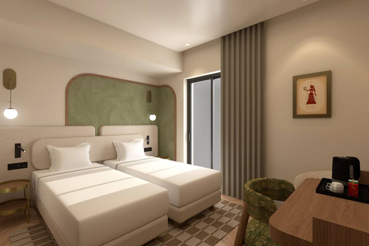 A hotel room with two beds, a desk, a chair, a coffee maker, and a framed picture on the wall.