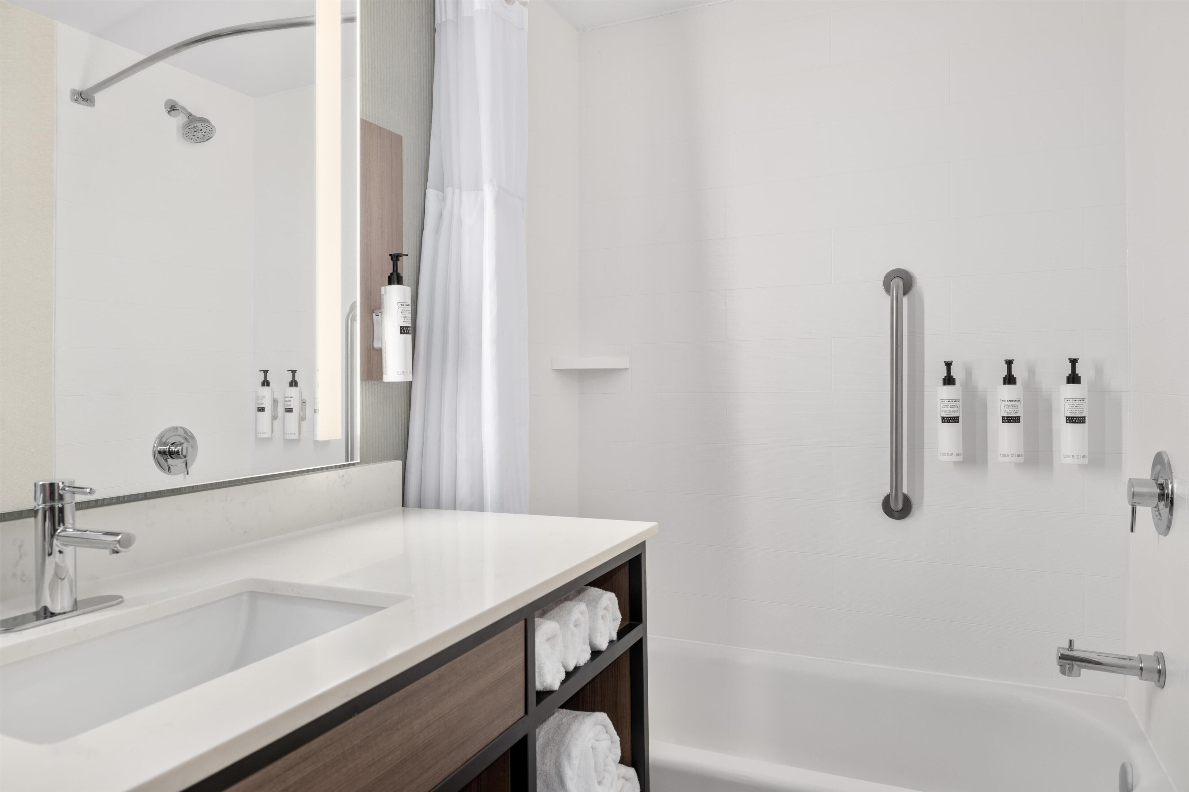 A modern bathroom with a large mirror, two sinks, a shower, and a bathtub.