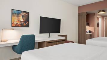 A hotel room with a bed, a desk with a computer monitor, a chair, and a painting on the wall.