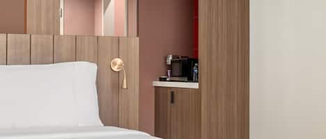 A hotel room with a bed, a bedside table, a microwave, and a water bottle.