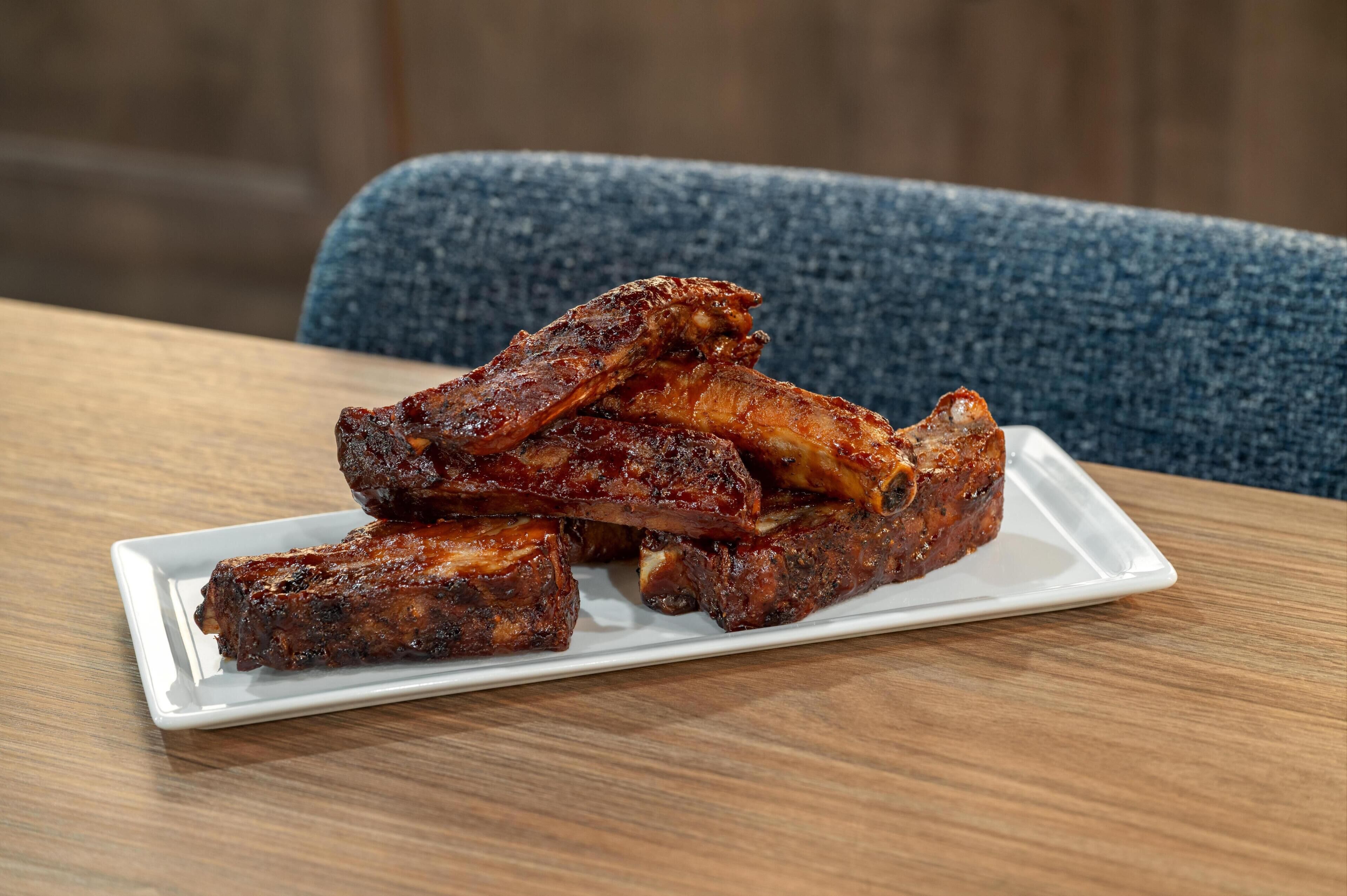 A white rectangular plate with barbecued ribs on a wooden table.