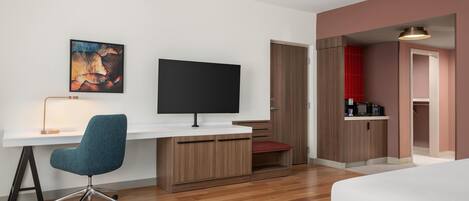 Una habitación de hotel moderna con escritorio, silla, televisión y una pequeña kitchenette.