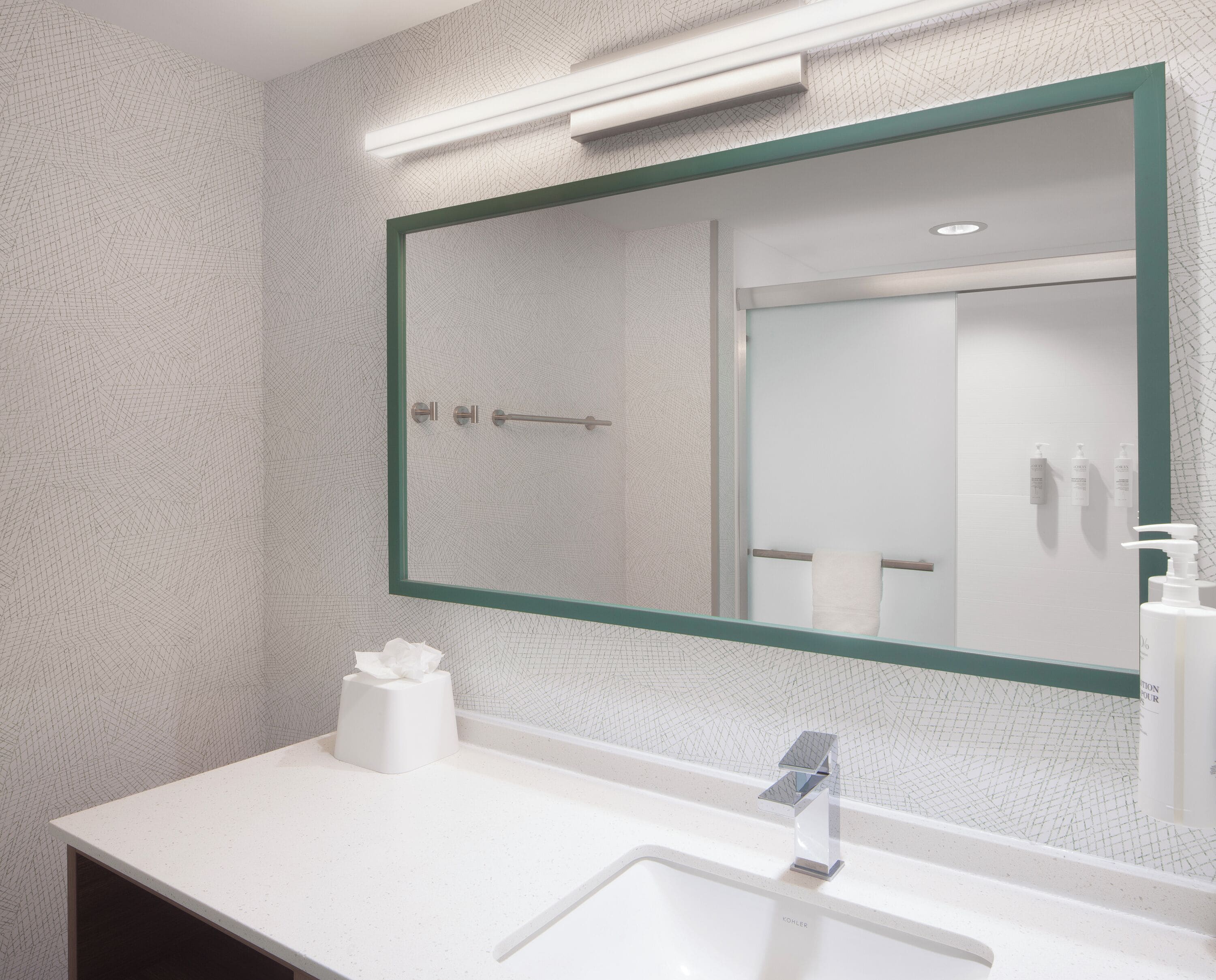 Een moderne badkamer met een grote spiegel, een wit aanrecht en een handdoekdispenser.